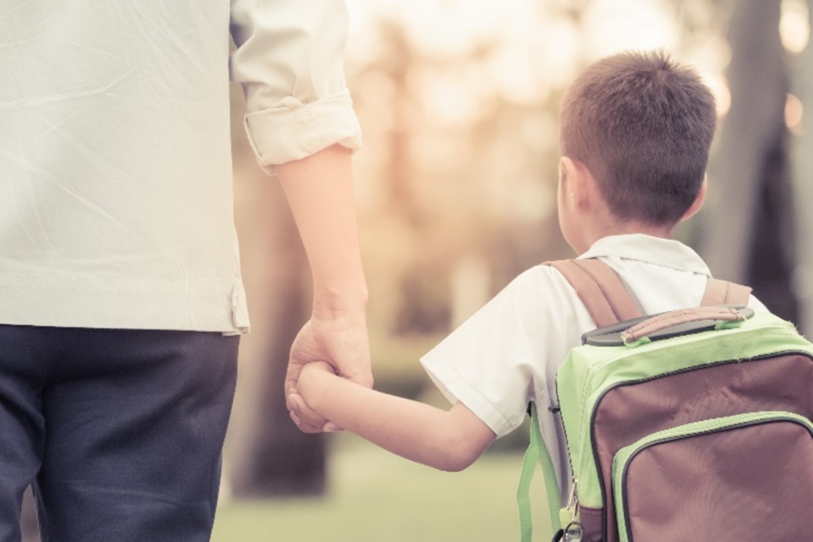 young child holding their parent's hand on their way to school