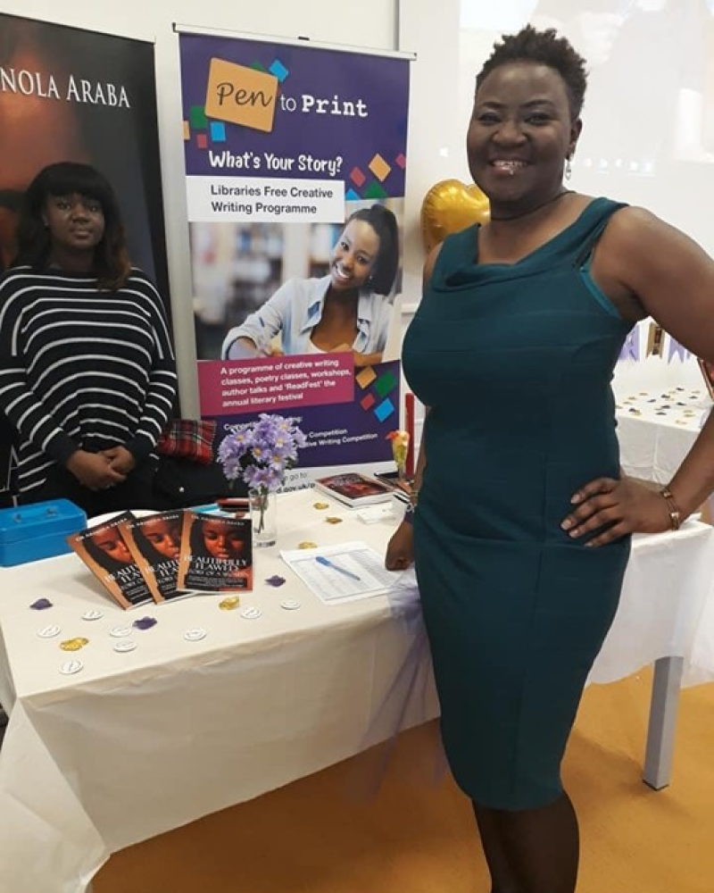 Black woman standing in front of a table that showcasing her books
