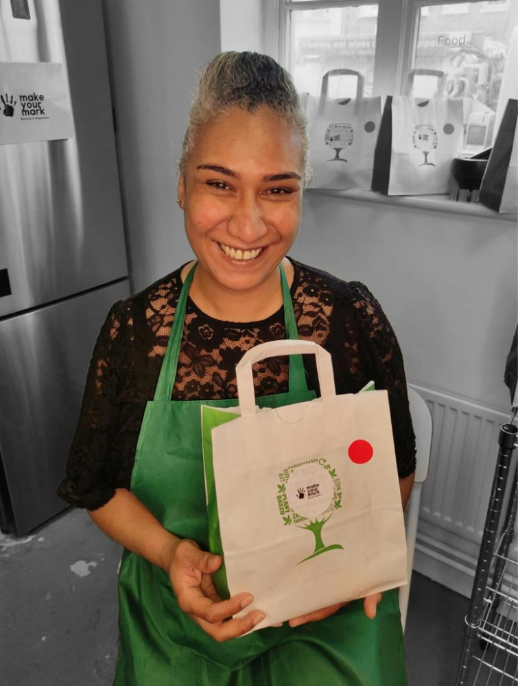 Black woman wearing an apron, holding a shopping bag smiling in the camera