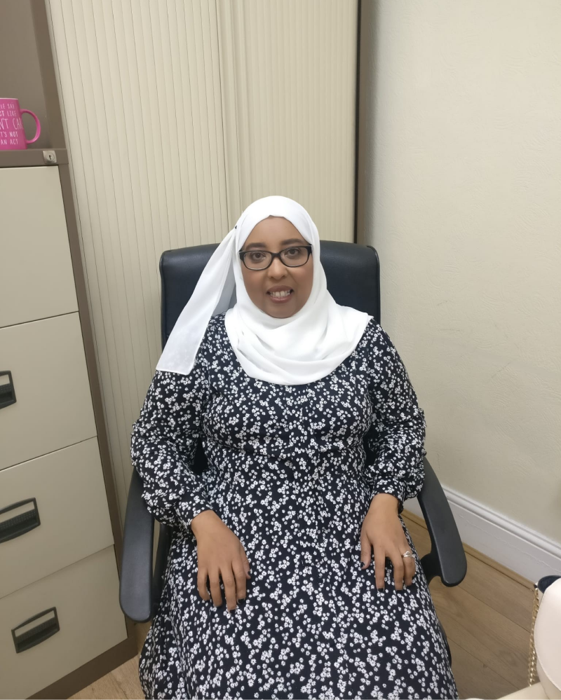 Black woman, who is wearing a hijab sitting in a chair looking into the amera