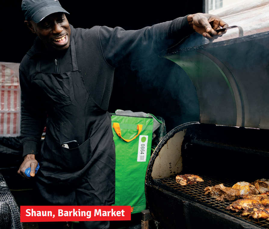 Smiling black man happily shows the cooking chicken in the open grill. Text says: 'Shaun, Barking Market'