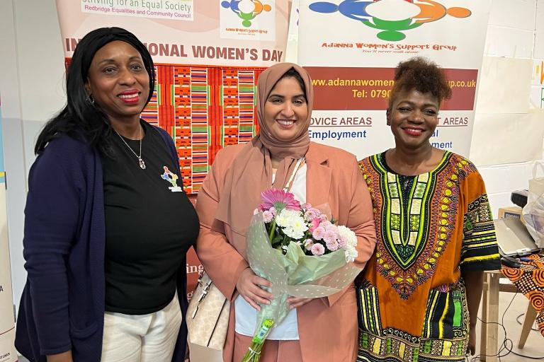Three women smiling to the camera, the middle one holding a bouquet of flowers