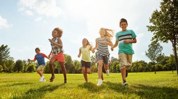 group of diverse kids running on grass surrounded by greenery