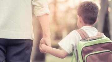 young child holding their parent's hand on their way to school 