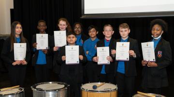 pupils on stage at dagenham park holding up arts award discover certificates