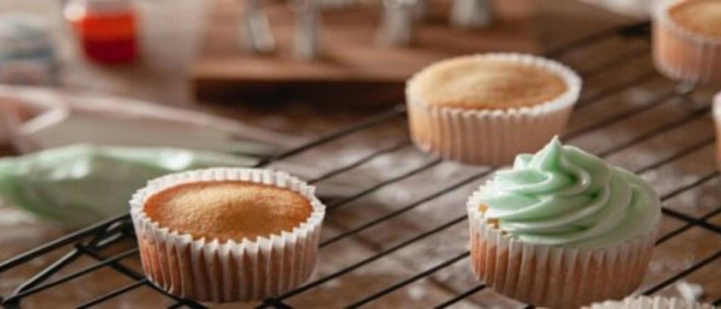 Image of cupcakes on a cooling rack. Some are iced and some are not. 