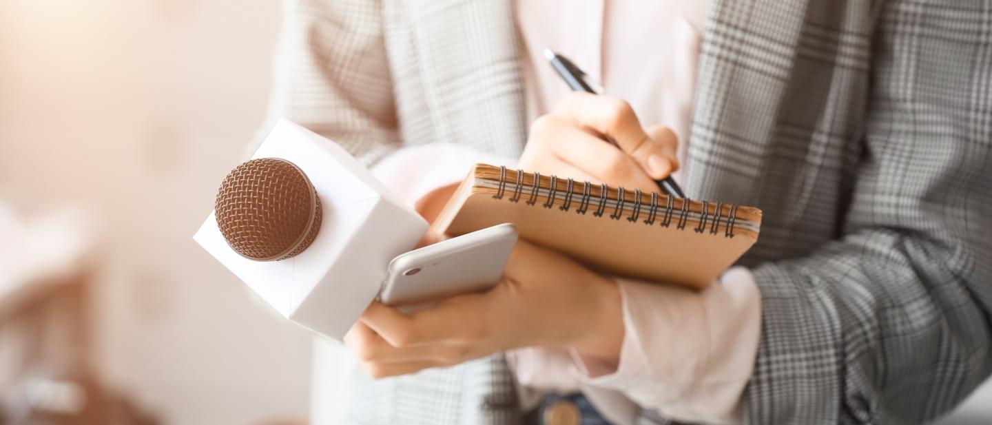 Shot of a person's hands holding a microphone while writing something in a notebook