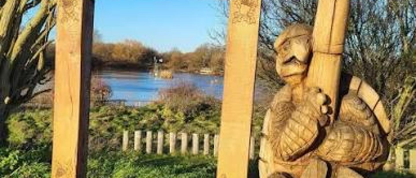 A large easel and figure of a painter carved out of wood standing next to a lake
