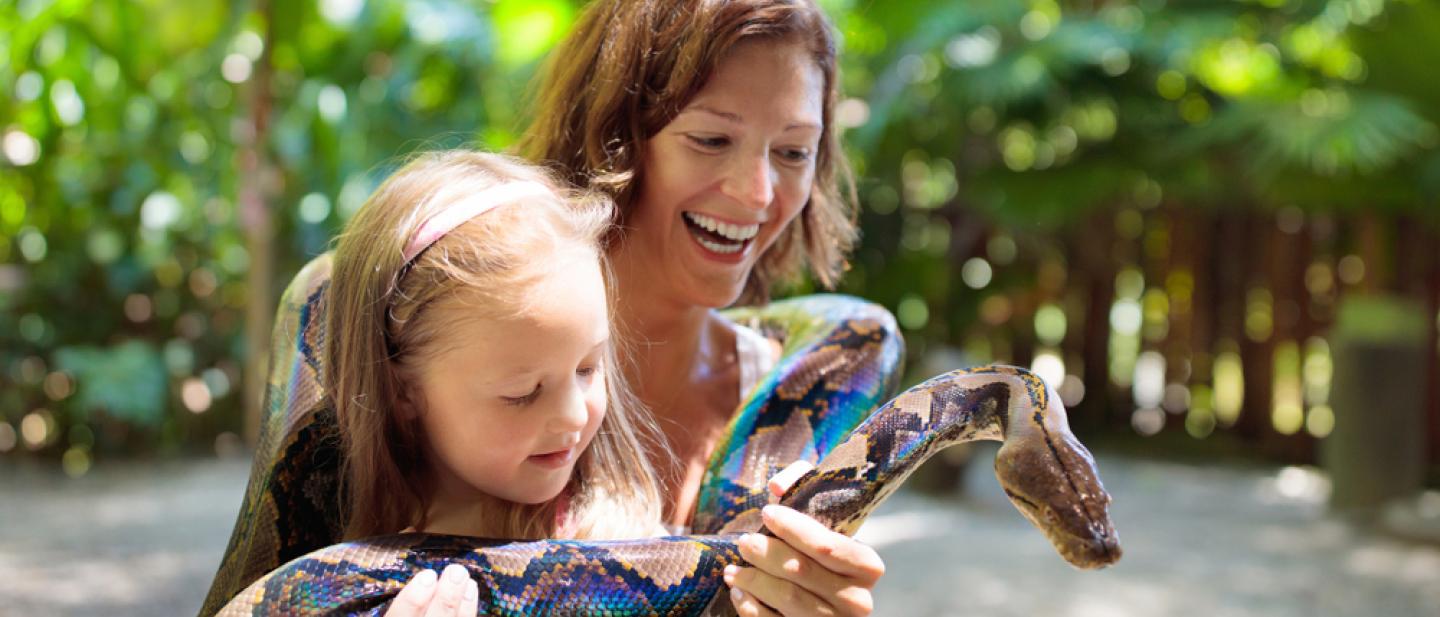 A woman holding a child, both smiling while a boa snake is wrapped around them