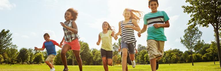 group of diverse kids running on grass surrounded by greenery
