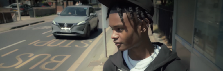 Young man standing at bus stop in Dagenham