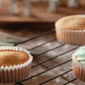 Image of cupcakes on a cooling rack. Some are iced and some are not. 