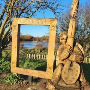 A large easel and figure of a painter carved out of wood standing next to a lake