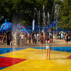 A young child is standing under water in a colourful waterpark pool